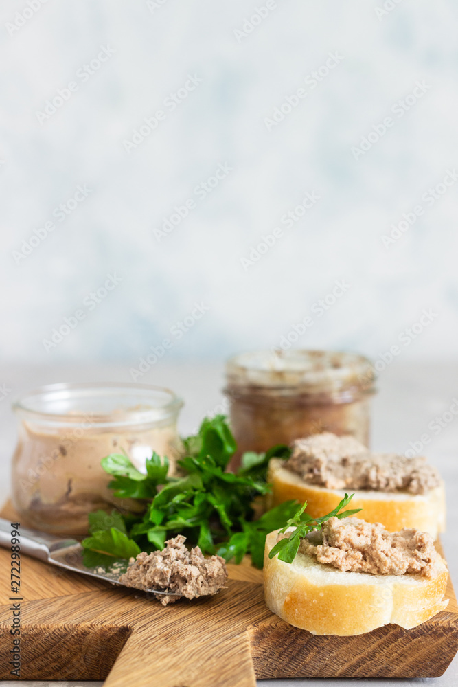 Liver pate in a glass jar with fresh bread and parsley on a wooden cutting board. Light grey stone background. Liver pate in a glass jar with fresh bread and parsley on a wooden cutting board. Light grey stone background.