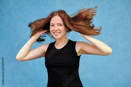 Photo portrait of a beautiful young pretty girl with dark red hair on a blue background in a black sweater. It stands directly in front of the camera in various poses, smiling, happy with life.