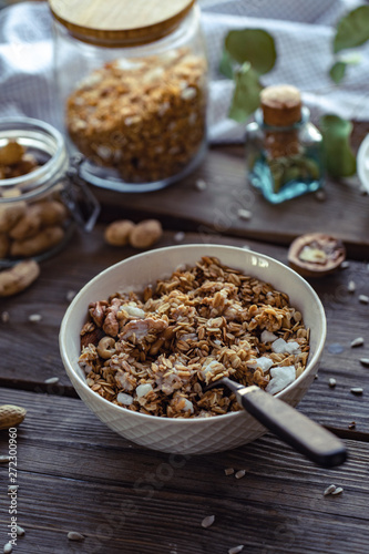 Granola morning breakfast bowl with spoon on brown wooden table background, healthy muesli food concept, cereal meal with nuts seed organic diet oat meal for health care, vertical close up view