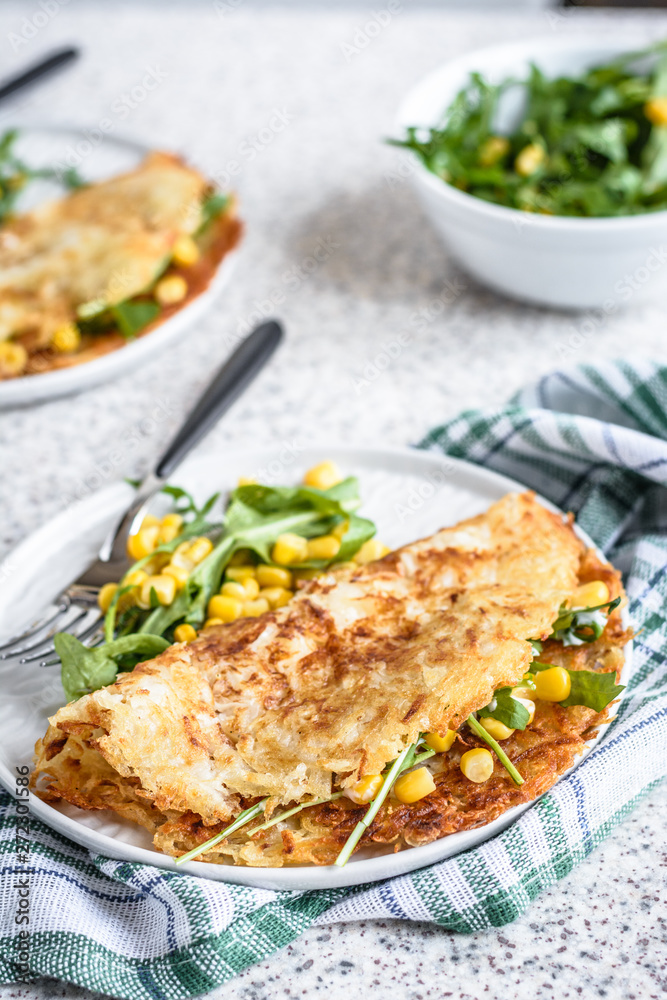 Potato rosti with corn and rocket salad served on a gray background. Traditional swiss dish Potato rosti with corn and rocket salad served on a gray background. Traditional swiss dish
