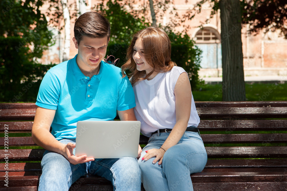 Happy young couple using laptop computer sitting on bench in city outdoor - Concept of relationship and people addicted to technology Happy young couple using laptop computer sitting on bench in city outdoor - Concept of relationship and people addicted to technology