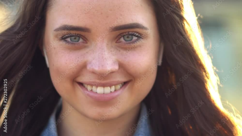 Close up portrait of Young Brunette Woman smiling at sunset, Girl wearing blue jeans jacket, sunbeams in hair. Slow motion. Close up portrait of Young Brunette Woman smiling at sunset, Girl wearing blue jeans jacket, sunbeams in hair. Slow motion.