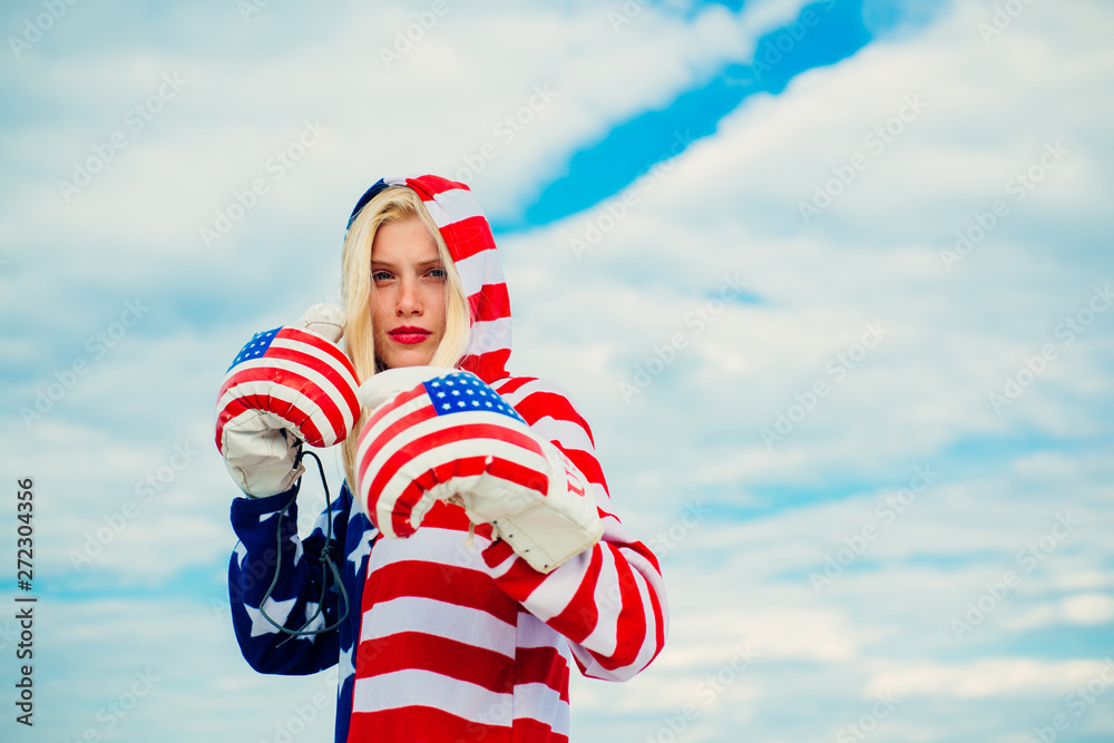 Obraz premium Boxer woman is getting ready to strike, wearing in red, white and blue costume, celebrating United States of America Independence Day. Brave American patriot adult girl in a 4th of July.