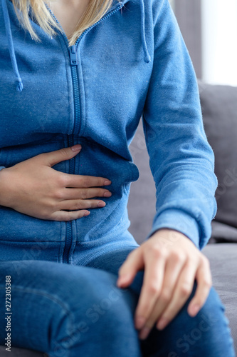 A girl holds her hand on a sore stomach while sitting at home on the couch