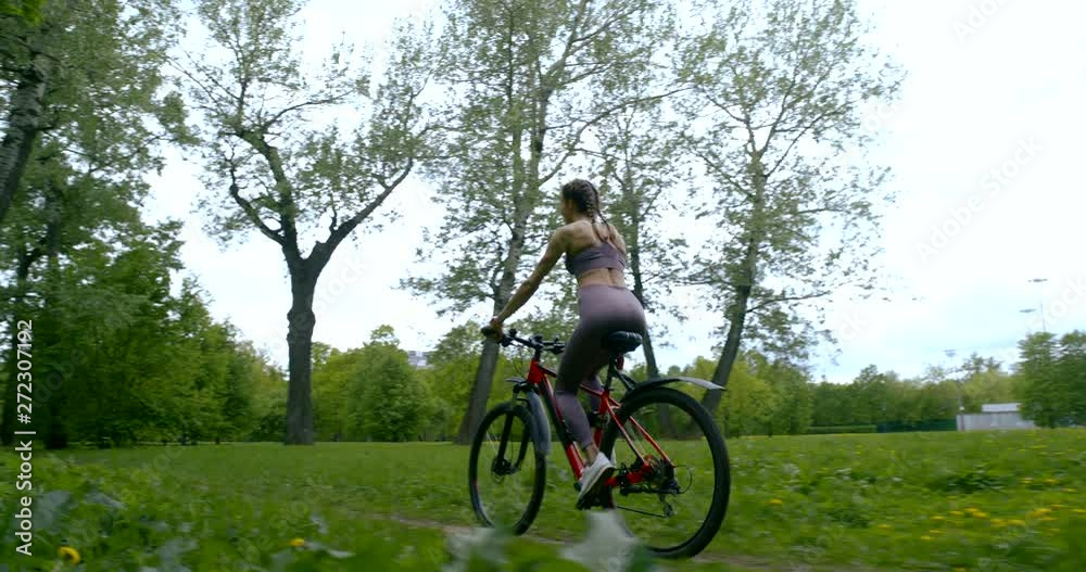 A beautiful slender girl in a t-shirt and leggings rides a Bicycle along the path among the trees and green grass. A beautiful slender girl in a t-shirt and leggings rides a Bicycle along the path among the trees and green grass.