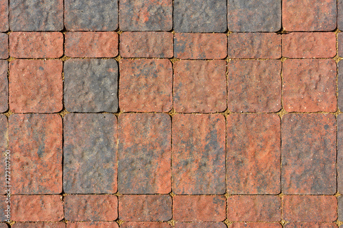 The surface is paved with road tiles of different sizes (multiformat). The uneven (melange) color of the tile makes it look like a natural stone. View from above.