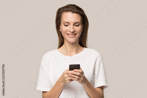 Smiling young woman using cellphone, looking at screen, chatting online