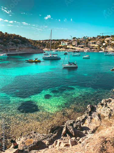 Panorama view of a beach bay with turquoise blue water and sailing boats and yachts at anchor with framed pine trees. Lovely romantic Cala Portals Vells, Mallorca, Spain. Balearic Islands 