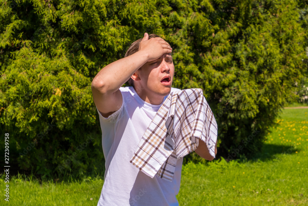 portrait of men sneezing from allergy, in a white T-shirt, stands in the park portrait of men sneezing from allergy, in a white T-shirt, stands in the park