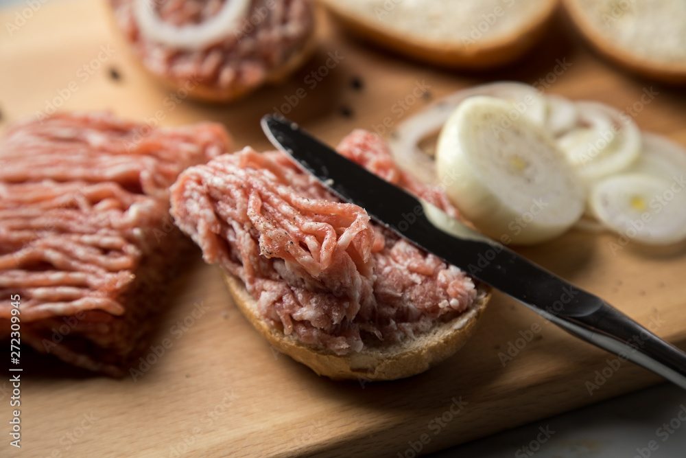 Deutsche Mettbrötchen mit rohen Schweine Mett, Brötchen, Butter, Zwiebeln, Pfeffer und Mett auf Holzbrett mit Messer in Küche