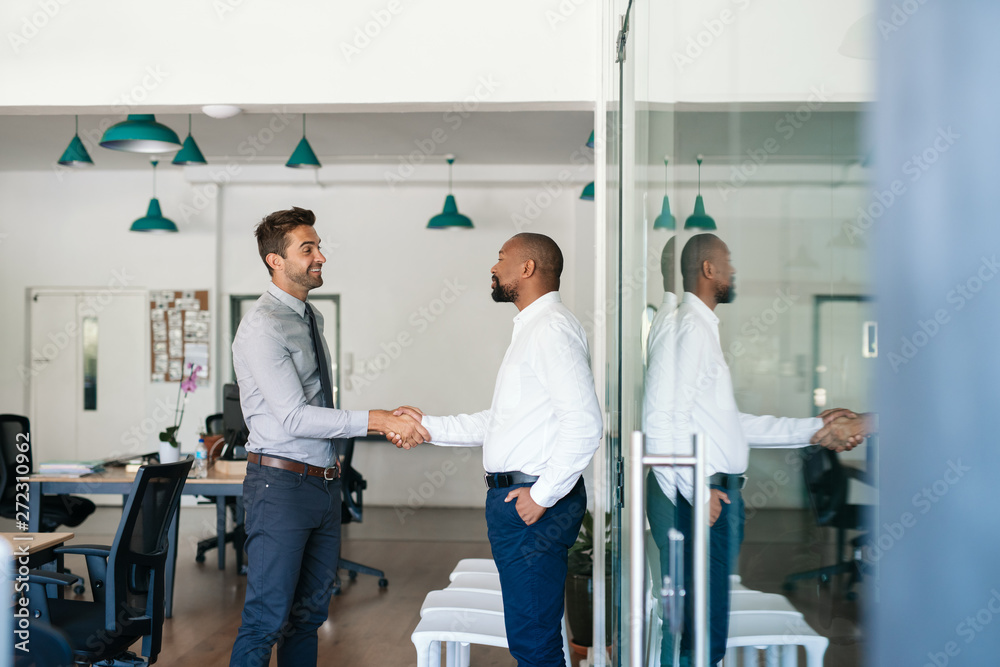 Two smiling businessmen shaking hands together after an office meeting