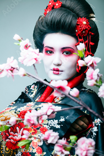 young pretty geisha in black kimono among sakura, asian ethno closeup