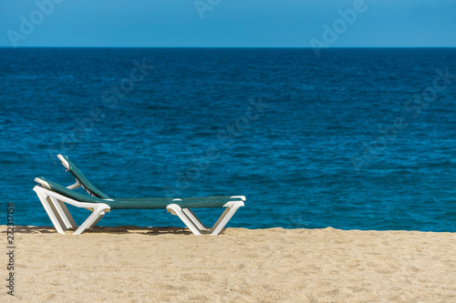Sun lounger on sandy beach with turquoise sea and blue sky