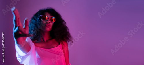Fashion young african girl black woman wear stylish pink glasses dance look at camera shoot hand gun isolated on party disco purple studio background, banner for website design, portrait, copy space © insta_photos