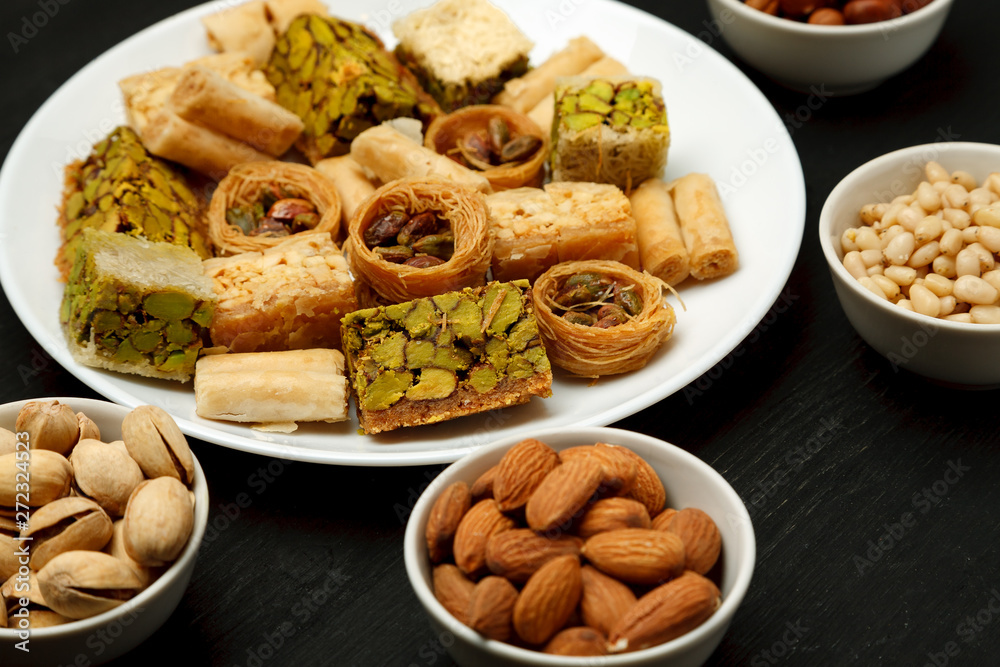 Traditional oriental sweets in white plate with different nuts on a black table, close-up shot