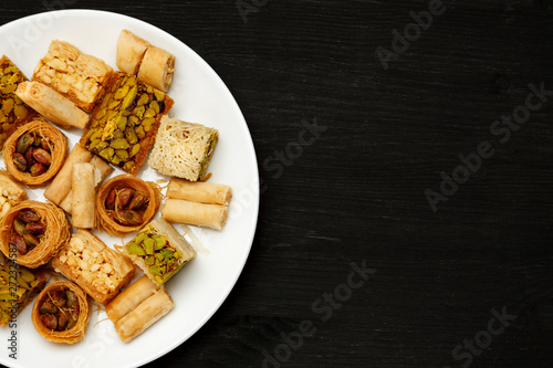 Traditional oriental sweets in white plate with different nuts on a black table, top view, copy space