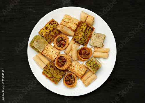Traditional oriental sweets in white plate with different nuts on a black table, top view