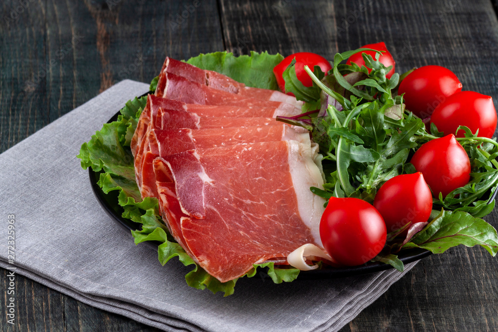 Plate with sliced jamon, tomatoes and herbs on a wooden table