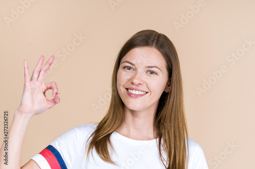 Portrait of adult girl smiling, looking at camera and showing ok sign