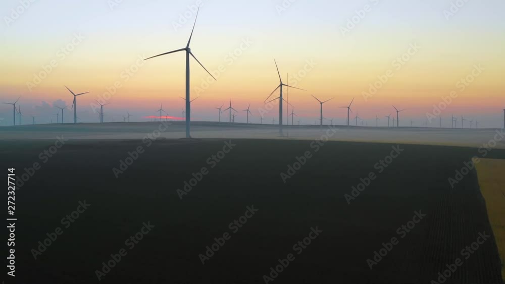 Aerial view of Eolian generators in a beautiful wheat field. Eolian turbine farm. Wind turbine silhouette. Wind field turbines. Wind propeller. Electric power production. Green energy. Sunrise light Aerial view of Eolian generators in a beautiful wheat field. Eolian turbine farm. Wind turbine silhouette. Wind field turbines. Wind propeller. Electric power production. Green energy. Sunrise light