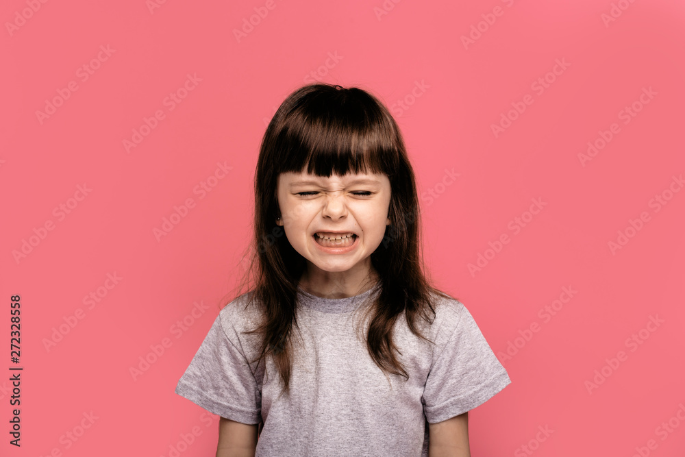 Close-up portrait of angry little girl with crazy emotional expression looking at camera with closed eyes, isolated on pink background. Naughty character. Problems of young parents. Horizontal image Close-up portrait of angry little girl with crazy emotional expression looking at camera with closed eyes, isolated on pink background. Naughty character. Problems of young parents. Horizontal image