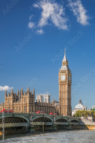Big Ben and Houses of Parliament with red buses against boat in London, England, UK