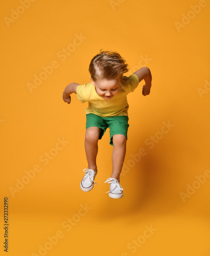Full length portrait of an excited young boy jumping leaping in green shorts over yellow  © Dmitry Lobanov