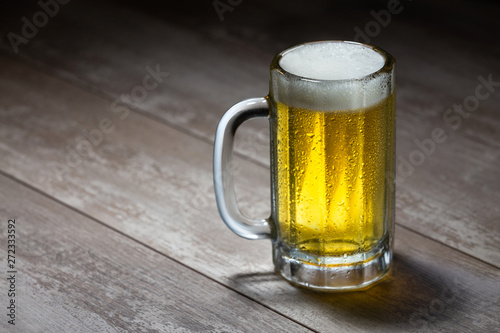 Fototapeta Delicious bright beer stein with frothy foam, poured fresh from the tap, on wood