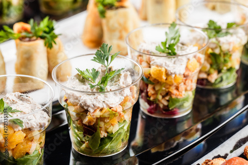 Photo Delicious appetizers with salmon, shrimp, cheese and greens in glass cups on banquet table