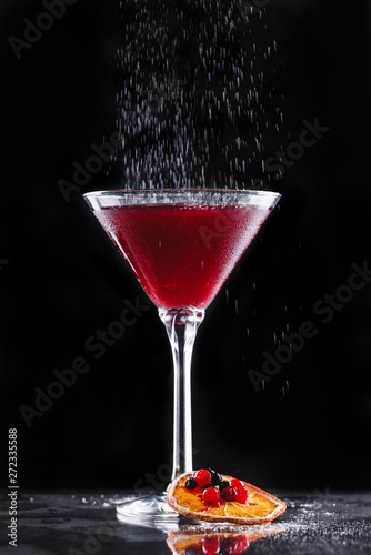 Cold red cocktail with red currant and powdered sugar in tall glass on black background. Summer drinks and alcoholic cocktails in motion