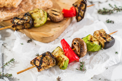 Grilled vegetable kebabs on skewers with zucchini, pepper, mushrooms, squash and herbs on paper over light table. Healthy vegan food, shashlik food photo