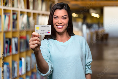 Smiling college university student holding mockup new bank credit card in library to assist her through education photo