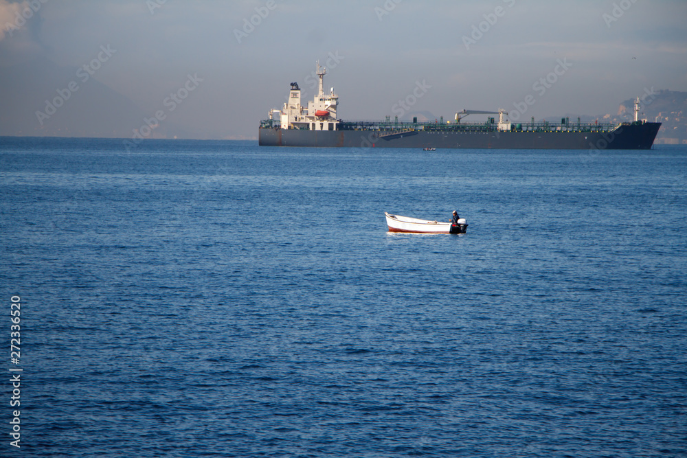 Unrecognizable man sailing on a boat with oars in the sea, a fisherman in a boat over a huge liner