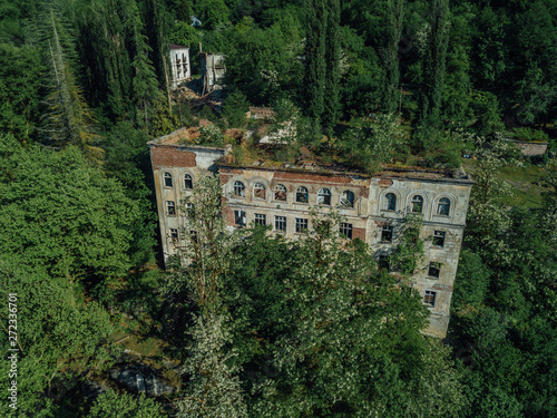 Ruined overgrown school in ghost mining town Akarmara, consequences of war in Abkhazia, aerial view from drone