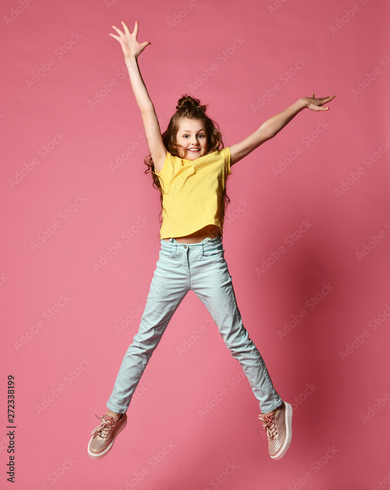 Smiling young girl or teen girl in jeans and yellow t-shirt have fun  jumping high with her arms and legs spread Stock Photo | Adobe Stock