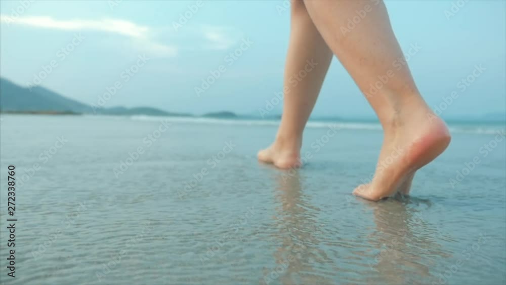 On a Tropical Beach Beautiful Scene of a Woman Walking on Ocean Beach at Sunset. Close-Up of Women's Legs European Beautiful Brunette, Walking Along the Beach, Slow Motion. On a Tropical Beach Beautiful Scene of a Woman Walking on Ocean Beach at Sunset. Close-Up of Women's Legs European Beautiful Brunette, Walking Along the Beach, Slow Motion.