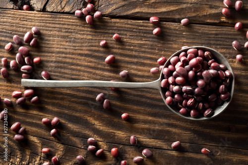 Raw, uncooked, dried adzuki (red mung) beans in metal spoon on rustic wood table background top view flat lay photo