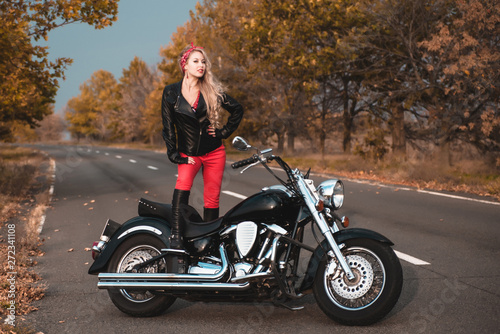 Beautiful biker woman posing with motorcycle on the road.