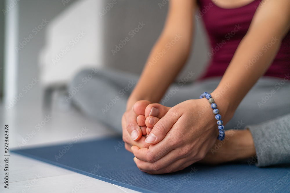Yoga leg stretches woman at home. Seated butterfly legs stretch holding soles of feet together. Closeup of hands holding barefoot feet on exercise mat. - obrazy, fototapety, plakaty 