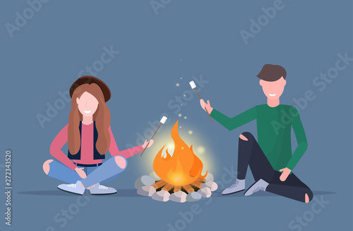 Couple hikers roasting marshmallow candies on campfire