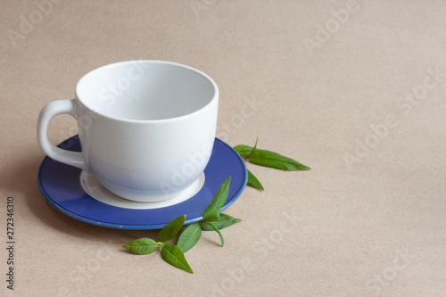 White cup and saucer placed on brown paper with mint leaves. Drinking object concept.