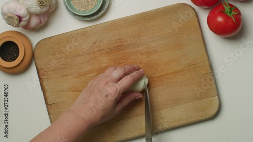 Hands chopping a garlic on a wooden board.