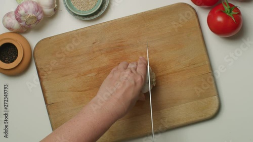 Hands chopping a garlic on a wooden board.