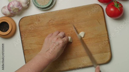 Hands chopping a garlic on a wooden board.