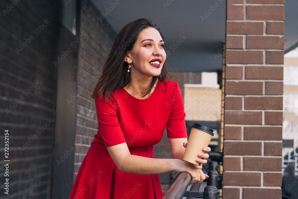 happy beautiful young woman with red lipstick in red dress holding takeaway cup of drink on the street happy beautiful young woman with red lipstick in red dress holding takeaway cup of drink on the street
