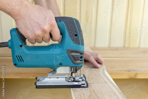 .A man is sawing a board with an electric jigsaw. A joiner's workshop. Copy space.