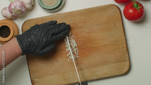 Hands with black sanitary PVC gloves, chopping a garlic on a wooden board.