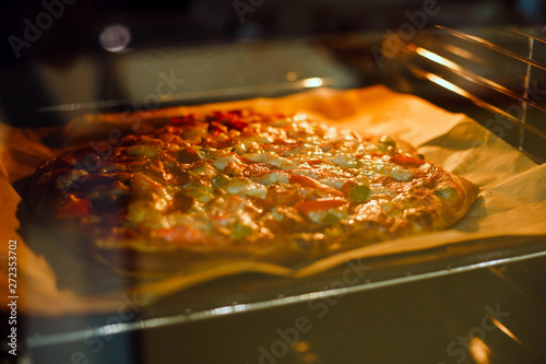 Homemade pizza is baked in the oven on a baking sheet and parchment paper. The view through the glass.
