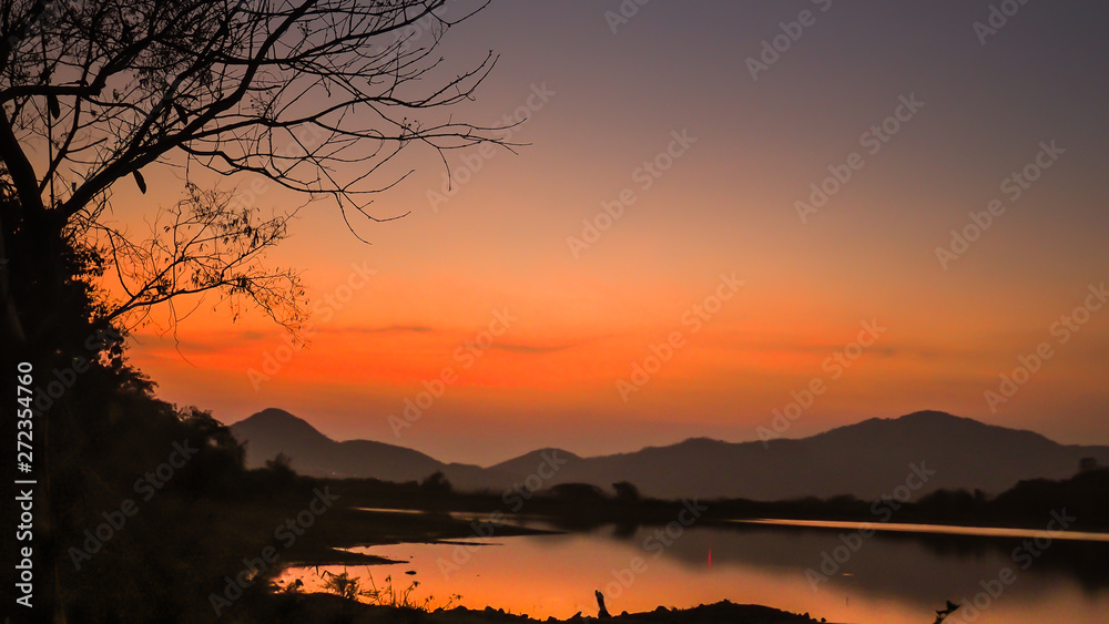 Obraz premium Landscape with orange and purple at sunset silhouettes of mountains, hills and forest lake