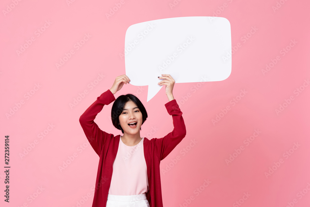 Smiling young Asian woman holding empty speech bubble in pink background Smiling young Asian woman holding empty speech bubble in pink background